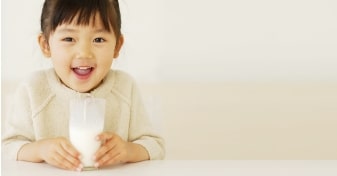 photo of a girl smiling and holding a glass of milk